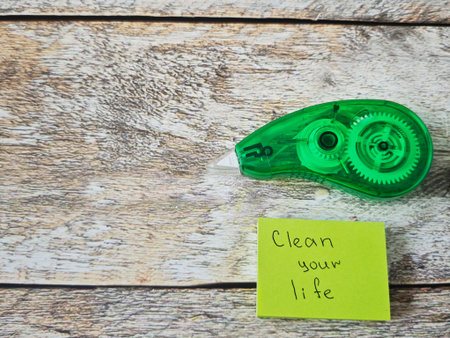 A green tape dispenser is placed on a wooden table surface. Next to it is a yellow note that says Clean your life. This scene shows an organized workspace in the afternoon.の写真素材