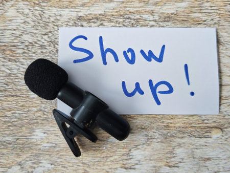 A microphone rests on a rustic wooden background beside a note that reads Show up. This captures the essence of speaking up, self-expression, and personal branding.の写真素材
