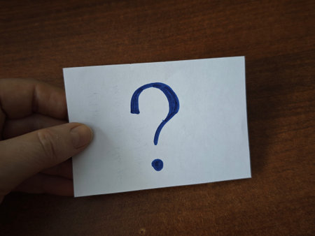A hand holds a card with a question mark drawn on it, symbolizing uncertainty and choices in...