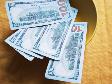 Kirov, Russia - February 20, 2026: Several hundred dollar bills are arranged on a round plate. The bills rest on a yellow cloth. Sunlight falls on the scene, highlighting the details of the currency.のeditorial素材