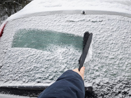 A person is using a brush to clear snow off the window of a car. Snow covers the vehicle and...