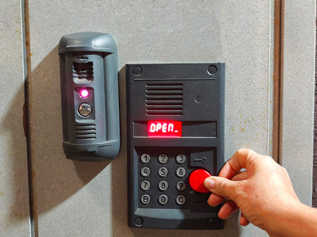 A person presses a red button to open a door with a keypad and a security device nearby in a...