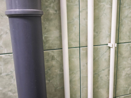 Interior plumbing setup shows water supply lines and sewer pipes along tiled walls in a bathroom or...