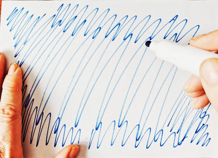 A person uses a marker pen to create blue lines on white paper. The lines are drawn in a quick and...