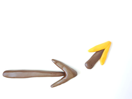 Two arrows made from clay point in different directions. One is brown and larger, while the other is...