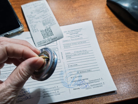 Kirov, Russia - February 27, 2026: A hand is holding a coin while a receipt and documents are on a...