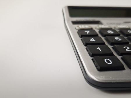 A calculator shows numbers and buttons on a surface as someone calculates during a task at home or...