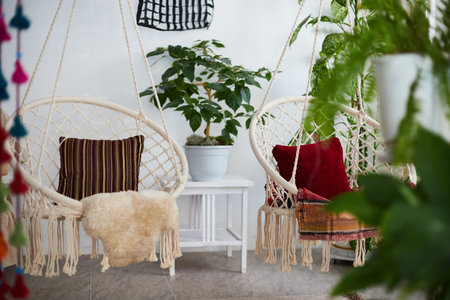 A bright interior features wicker hanging chairs with cushions, indoor plants, and a natural decor...