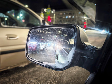 Traffic lights and cars in the distance are visible through a car mirror, creating a blurred view of the busy street at night.の写真素材