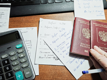 Kirov, Russia - February 02, 2026: A hand is holding two passports while documents and a calculator...