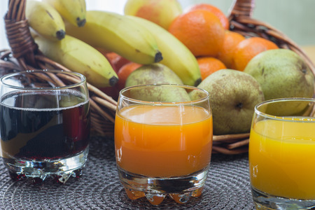multi fruit citrus juice from oranges, lemons, bananas, grapes in a glass with fruit basket in the backgroundの写真素材
