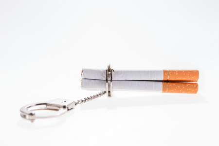 Addition concept with cigarettes and handcuffs on white backgroundの写真素材