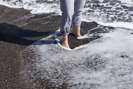 Woman with bare feet in water on the black beachの写真素材