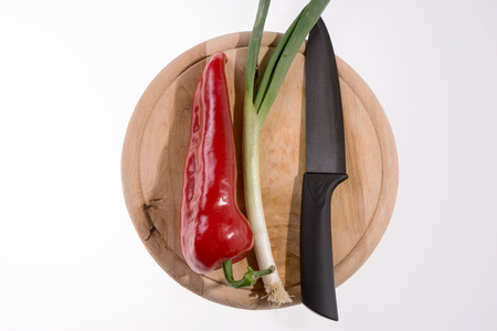 Pepper, spring onion and black knife on the wooden cutting boardの写真素材