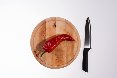 Fresh red paprika on the wooden cutting board and black knife isolatedの写真素材