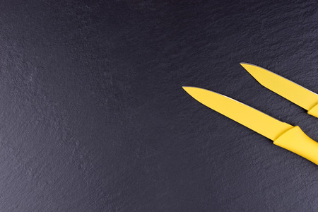 Two yellow kitchen knives on black slate plateの写真素材