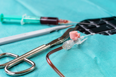 Scalpel, syringe, cannula and pair on scissors on green gauze with hole over the keyboardの写真素材
