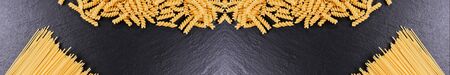 Panoramic image of yellow spaghetti on black slate plate. Copyspace