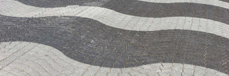 Wavy light and dark gray cobblestone pavement on the street. Panoramic image