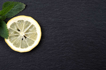 Top view of sliced yellow lemon with leaves of fresh lemon balm (Melissa officinalis) on black backgroundの写真素材