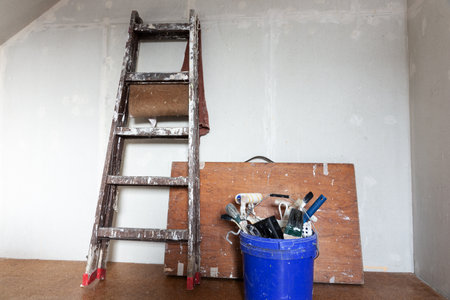 Painter equipment. Ladder and wooden table on the wall. Paint brushes and paint roller in the bucketの写真素材
