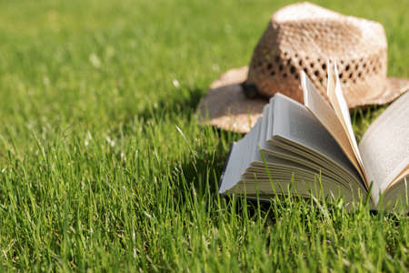 Open book lies on a lawn with straw hat in the background. Relaxation in the garden during  pandemicの写真素材