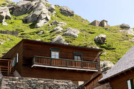 Square wooden house on the mountain with large stones in the background
