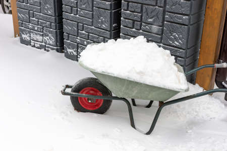 Wheelbarrow full of snow. Lots of snow on the sidewalk. Cleaning streets and roads by handの写真素材