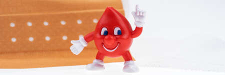 Drop of blood with a funny face in front of a medical plaster. Panoramic imageの写真素材