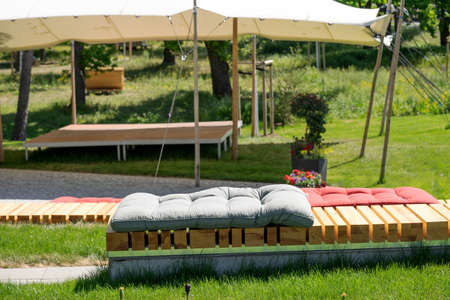 Empty wooden bench with cushions in front of a small stage with a tentの写真素材