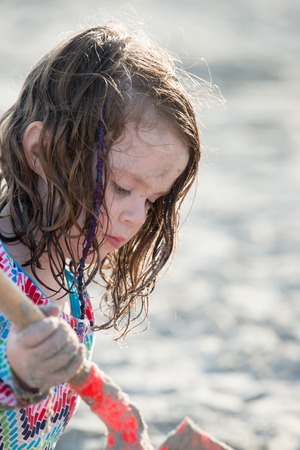 Young little girl playing with the sand and building sandcastle at the beach near the sea.の写真素材