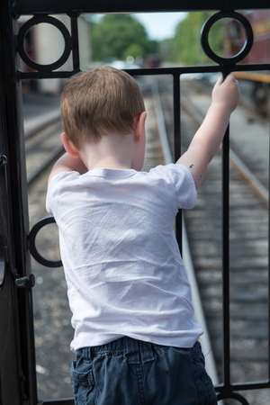 Young boy standing at back of train looking down at trackの写真素材