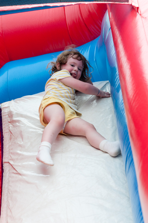 Young happy girl child riding inflatable slide outdoors on a warm summer day.の写真素材