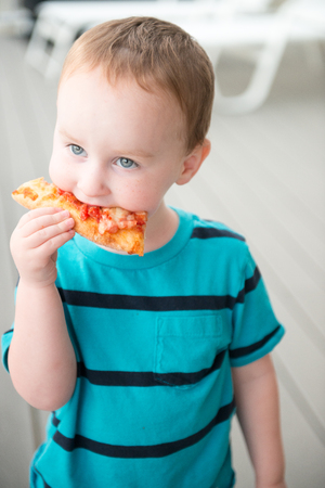Young toddler boy on patio deck outside at sunset down at shore eating pizzaの写真素材