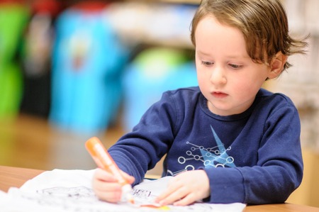 Young boy sitting down at desk indoors coloring with markersの写真素材