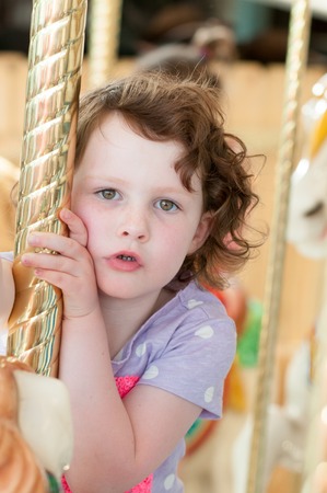 Young girl riding on fairground horse on carousel amusement ride at fairgrounds park outdoorの写真素材
