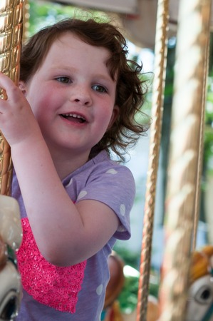 Young girl riding on fairground horse on carousel amusement ride at fairgrounds park outdoorの写真素材