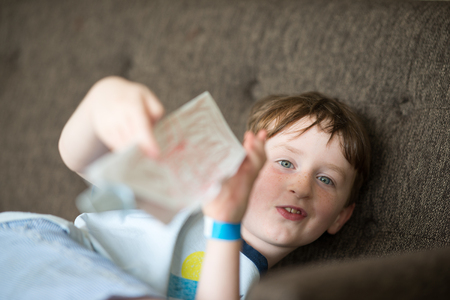 Young boy lying relaxing on a sofa while readingの写真素材