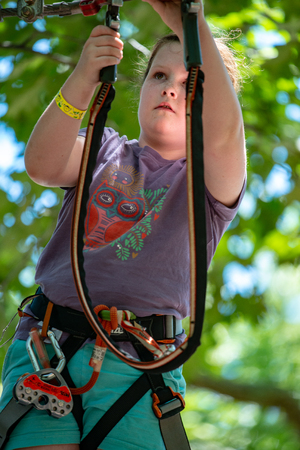 Portrait of a beautiful girl on a rope park among trees. Children summer activities.
