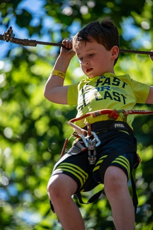 Portrait of a handsome boy on a rope park among trees. Children summer activities.