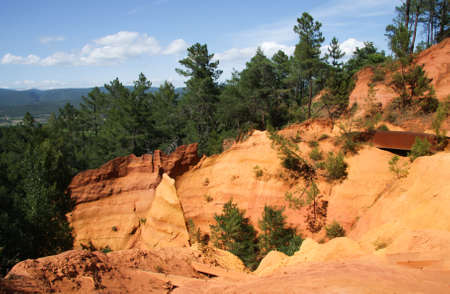 View of colorful orange ochre cliffs with pine trees and blue sky at the natural regional park in Roussillon, Vaucluse, Luberon, Franceの写真素材