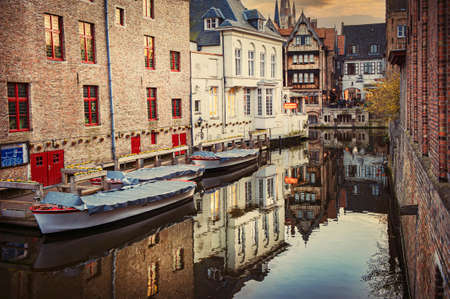 Romantic evening view of the canal, boats, old town buildings illuminated by the rays of the setting sun and reflections in the water, Bruges, Belgium. Can be used for websites, brochures, posters, printing and design.のeditorial素材