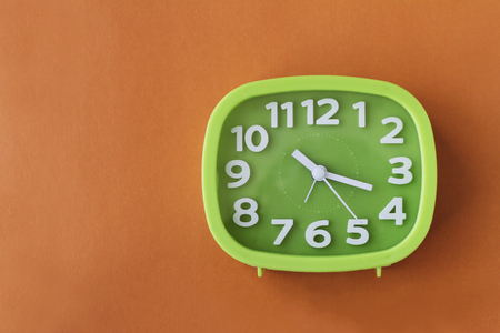 Green clock with white numbers and arrows on orange backgroundの写真素材