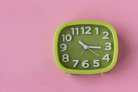 Green clock with white numbers and arrows on pink background