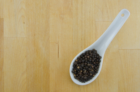 A spoon holds whole peppercorns on a butcher block background with copy spaceの写真素材