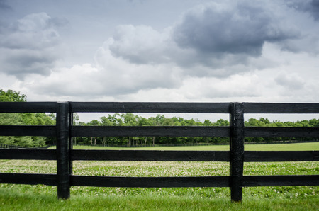 Black painted fence along a horse pasture right before a summer stormの写真素材