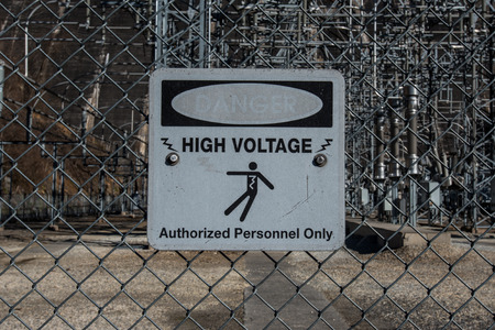 Faded high voltage danger sign on chainlink surrounding a power plant generating electricity from water flowの写真素材