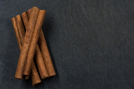 Three Cinnamon sticks on black slate background with copy space to rightの写真素材