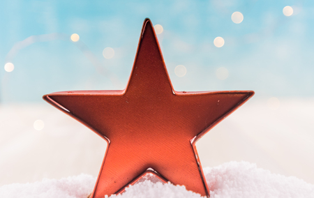 Orange Tin Star Ornament in Snow with light blue bokeh behindの写真素材