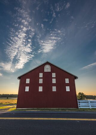 Cloudy Sunset Sky Above Red Barn Towering Over Roadの写真素材